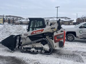 A Bobcat skid steer, essential snow removal equipment, parked in a snowy lot next to a Cities Lawn and Snow LLC truck in Woodbury, MN.