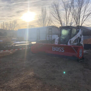 A Bobcat skid-steer loader equipped with a red BOSS snow plow, ready for heavy-duty snow removal by LAWN Sharks LLC in Colorado Springs, CO.