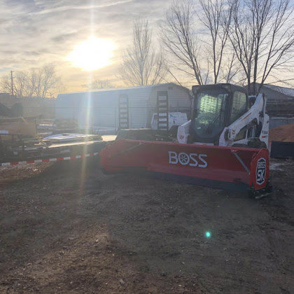 A Bobcat skid-steer loader equipped with a red BOSS snow plow, ready for heavy-duty snow removal by LAWN Sharks LLC in Colorado Springs, CO.