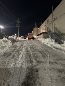 A Bobcat clearing snow from a commercial property at night by Lovett lawn care & snow removal in Omaha, NE.