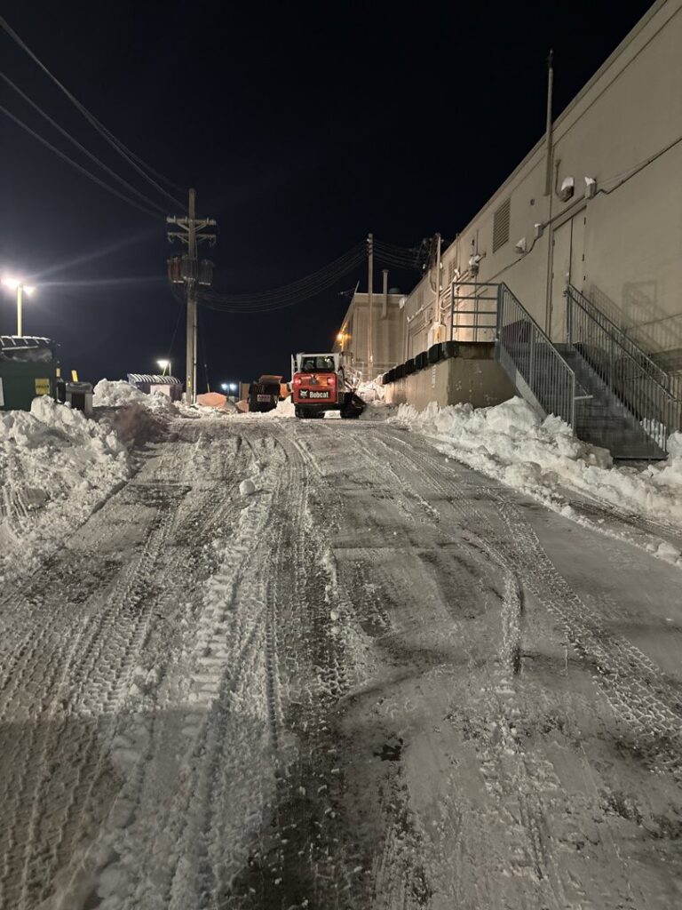 A Bobcat clearing snow from a commercial property at night by Lovett lawn care & snow removal in Omaha, NE.