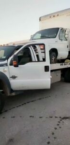 A white box truck loaded onto a flatbed tow truck operated by Geely Towing in Fargo, ND.