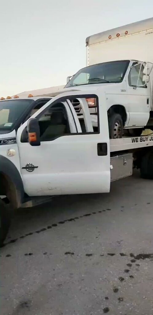 A white box truck loaded onto a flatbed tow truck operated by Geely Towing in Fargo, ND.