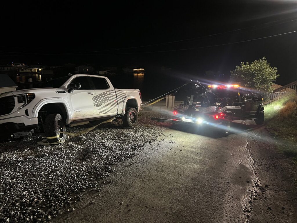 A B&R Towing and Automotive truck recovering a white pickup truck from a muddy area at night in Knoxville, TN.