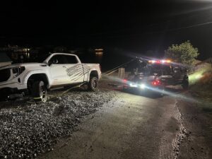 A B&R Towing and Automotive truck recovering a white pickup truck from a muddy area at night in Knoxville, TN.