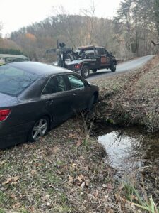 A B&R Towing and Automotive truck recovering a dark sedan stuck in a ditch in Knoxville, TN.