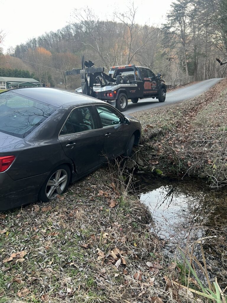 A B&R Towing and Automotive truck recovering a dark sedan stuck in a ditch in Knoxville, TN.