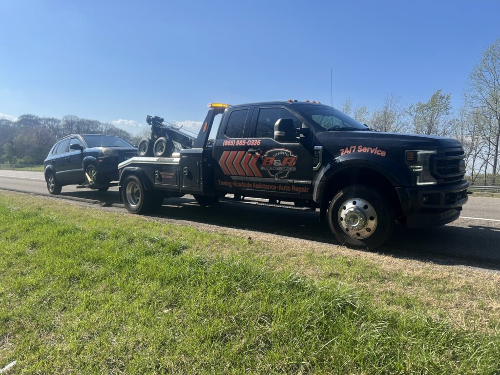 A B&R Towing and Automotive truck towing a dark SUV on a highway in Knoxville, TN.