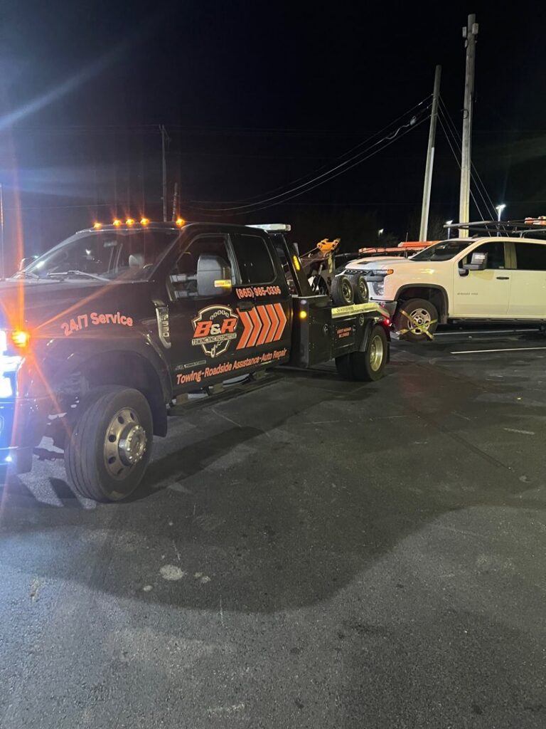 A B&R Towing and Automotive truck towing a white SUV at night in Knoxville, TN.