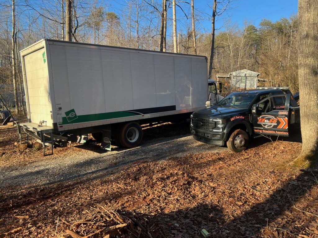 A B&R Towing and Automotive truck assisting a large white box truck in a wooded area in Knoxville, TN.