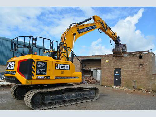 An excavator with a grapple attachment demolishing a brick building by The real wrecking crew in Broken Arrow, OK