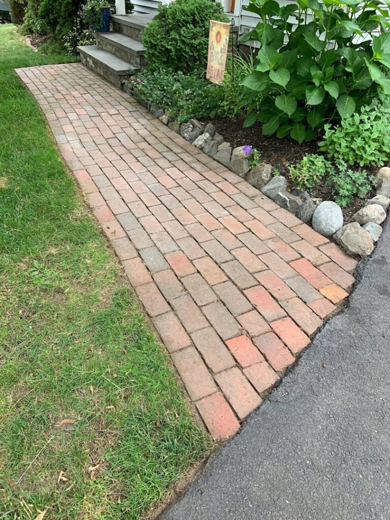 A brick pathway alongside a well-maintained lawn and garden by Steele Lawns in Portland, ME.