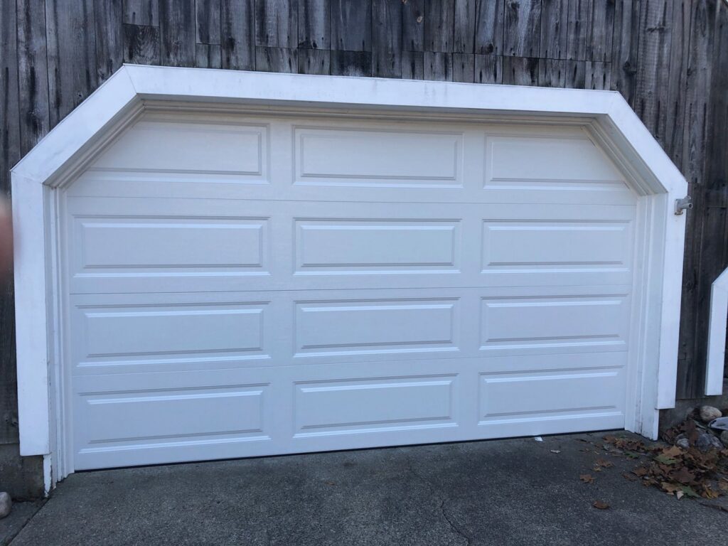 Two brown carriage-style garage doors with decorative hardware on a home with stone facade by Compton Doors, Inc. in Attleboro, MA