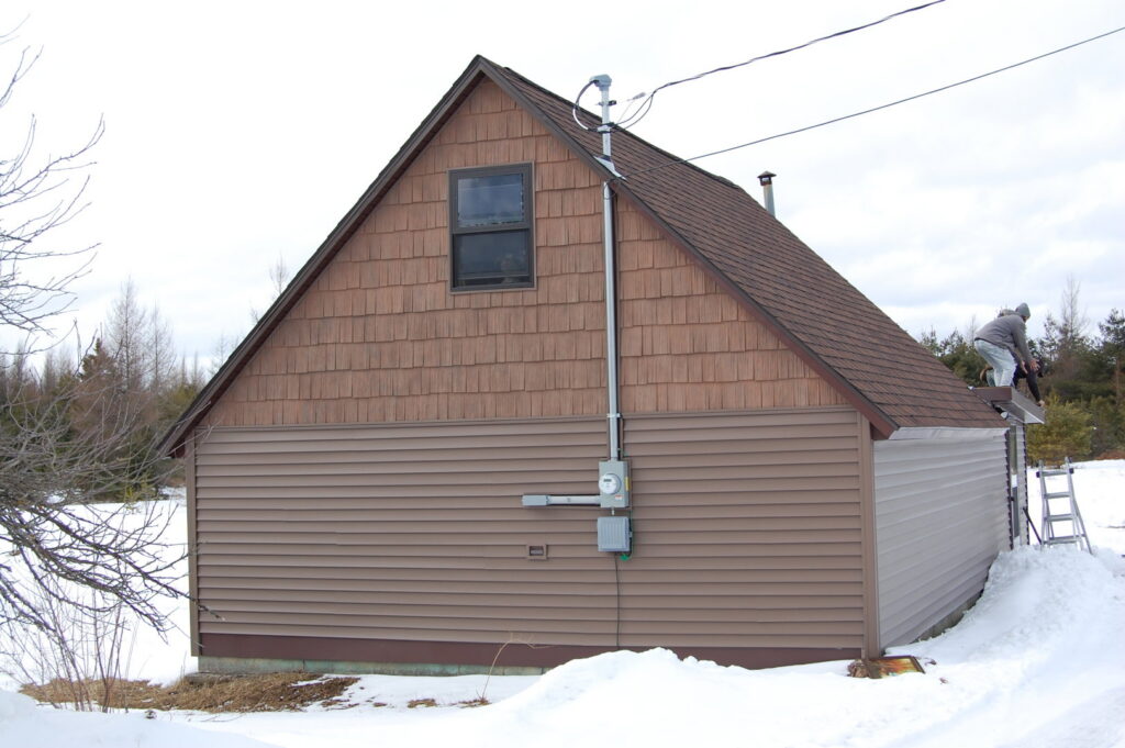 A house featuring brown horizontal siding and cedar shake siding on the gable, completed by Murphy Builders- Genesee County in Ossineke, MI.