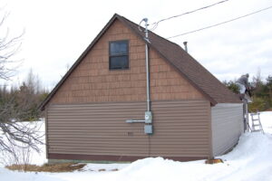 A house featuring brown horizontal siding and cedar shake siding on the gable, completed by Murphy Builders- Genesee County in Ossineke, MI.