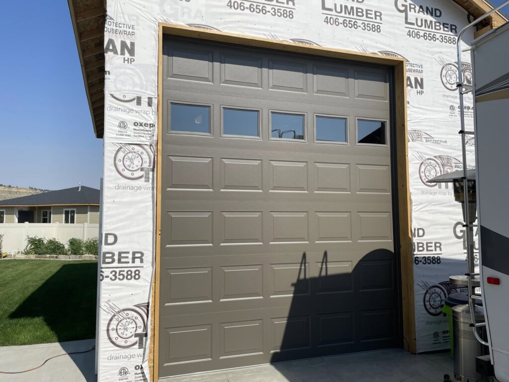 A brown panel garage door with windows installed on a new construction building by Elite Garage Door Service & Repair in Billings, MT.