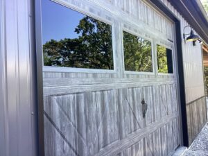 A brown wood-grain garage door with decorative windows installed by Fayetteville Garage Door Co. in Fayetteville, AR