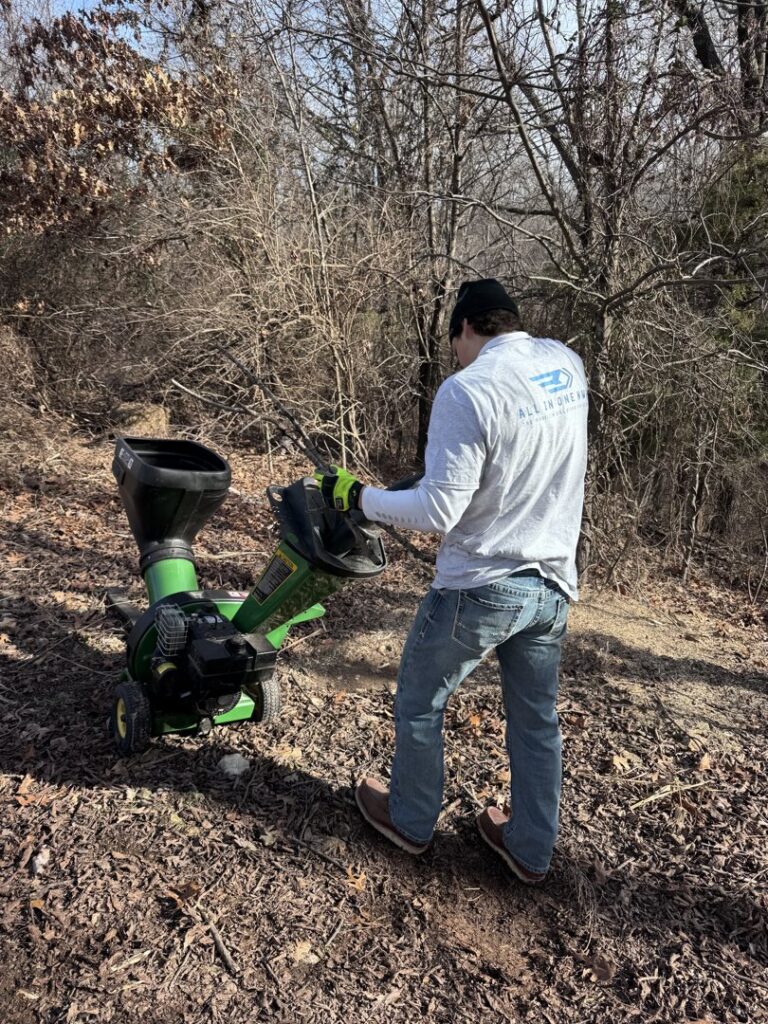 A worker operating a wood chipper for brush clearing by All in- Landscaping and Power-washing in Fayetteville, AR.