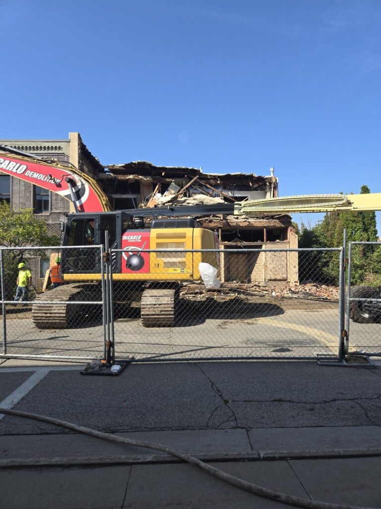 A building undergoing demolition by DeCarlo Demolition Company, viewed from behind a safety fence in Des Moines, IA.
