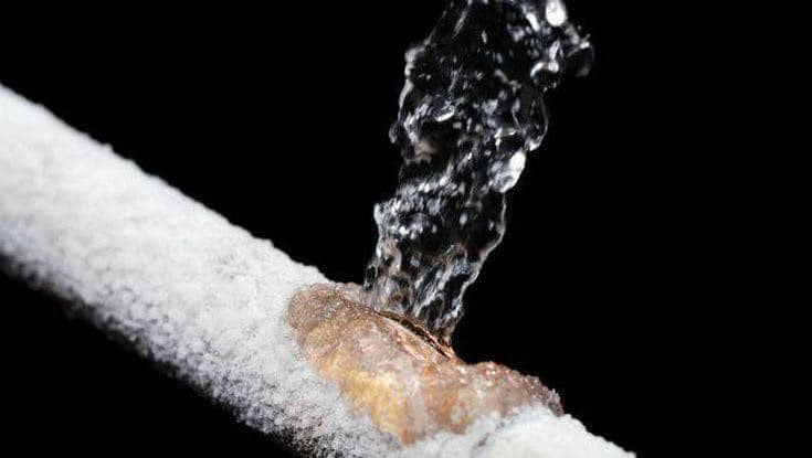 A close-up view of a burst and frozen pipe with water actively leaking, a common cause of water damage addressed by The Restoration Experts in Waupaca, WI.