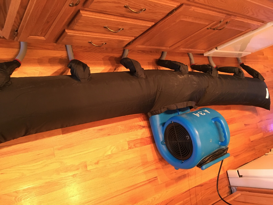 Drying equipment with a large air mover and tube used to dry water-damaged cabinets by AllStar Response in Manhattan, KS