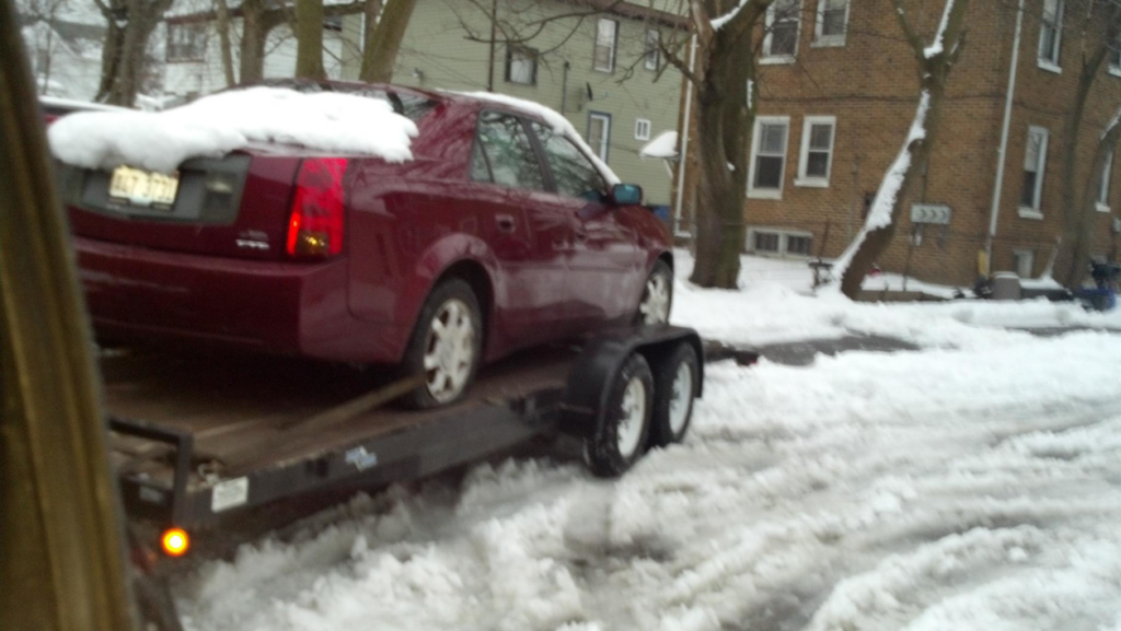 A red Cadillac car being towed on a trailer in snow by Jr & Sr towing and recovery in Waukegan, IL.