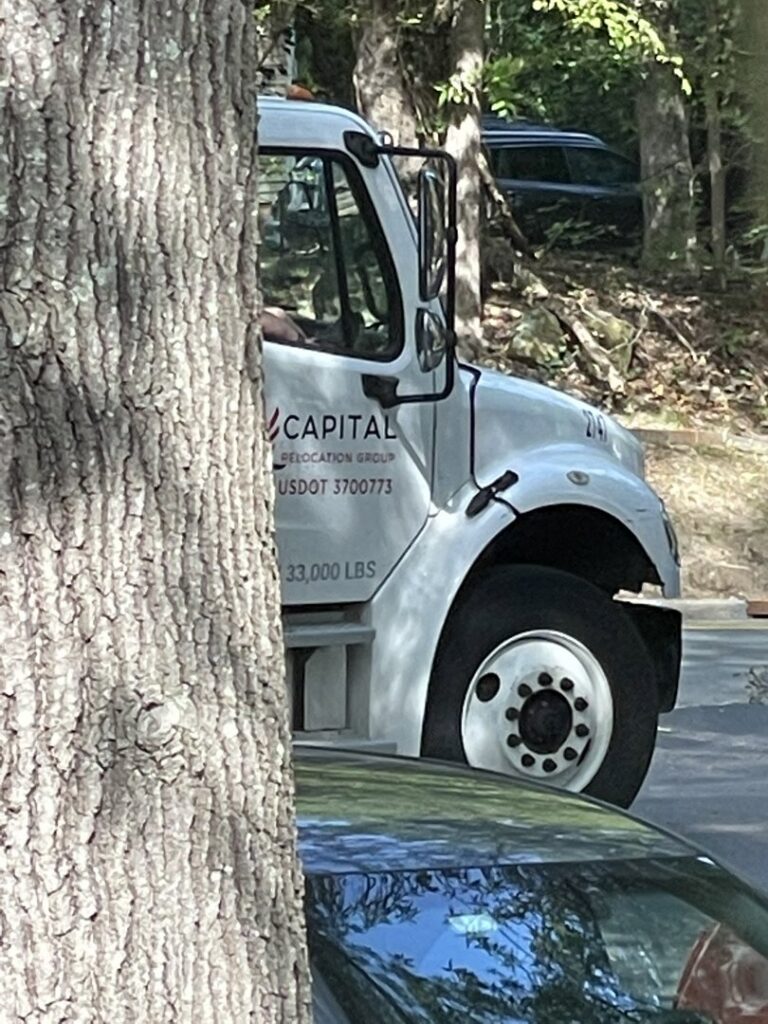 A Capital Relocation Group moving truck with branding visible, partially obscured by a tree in Raleigh, NC.
