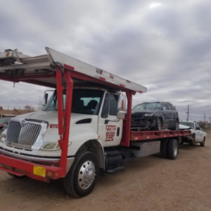 A car carrier tow truck from Gama Towing LLC transporting a damaged SUV and another vehicle in Carlsbad, NM.