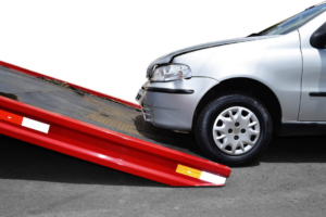 A silver car with minor damage positioned to be loaded onto a red flatbed tow truck by On Time Towing Houston, TX.