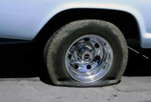 A car with a completely flat tire on the side of the road, indicating a need for roadside assistance or towing from Emergency Towing Sacramento, CA.