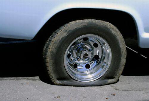 A car with a completely flat tire on the side of the road, indicating a need for roadside assistance or towing from Emergency Towing Sacramento, CA.