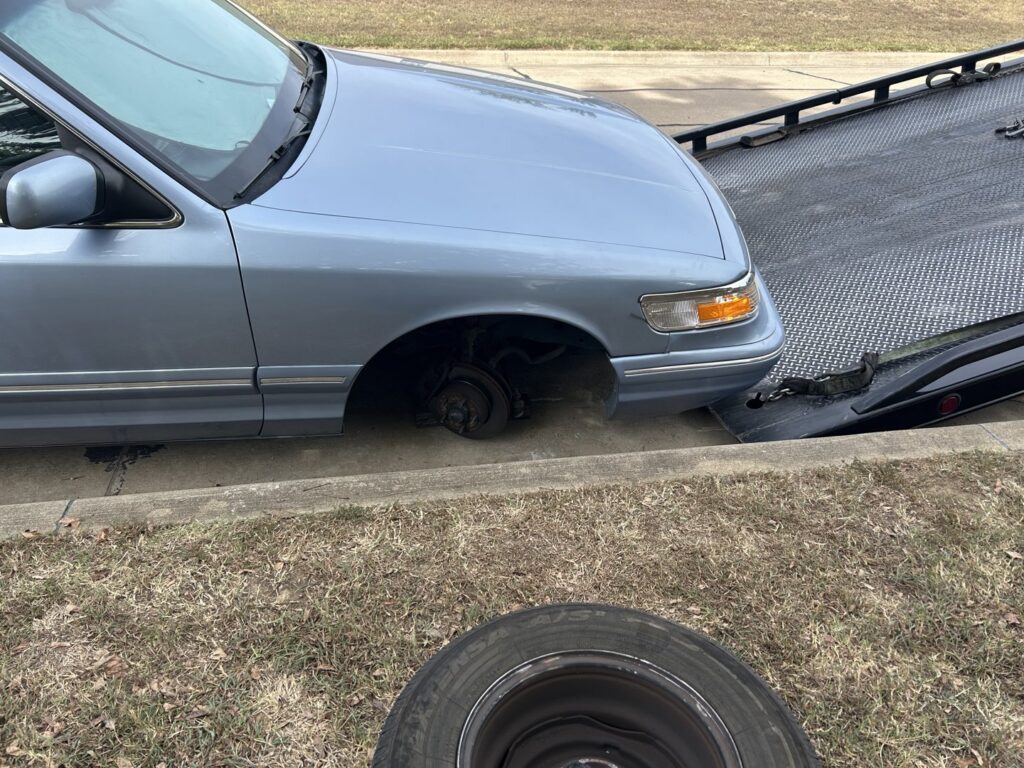 A light blue car with a missing wheel being prepared for towing by 918 Wrecker Service in Tulsa, OK.