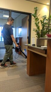 A professional cleaner from Leave The Dust To Me Cleaning Services LLC in Anchorage, AK, cleaning carpets in an office hallway.