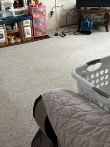 A carpeted room with an air mover in the background, indicating water damage drying by Southcoast Cleaning Solutions & Restoration in Fall River, MA.