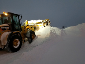 A yellow CAT loader with a snow pusher attachment moving a large snow pile for Rochester Ground Lawn & Snow Services in Rochester, MN.