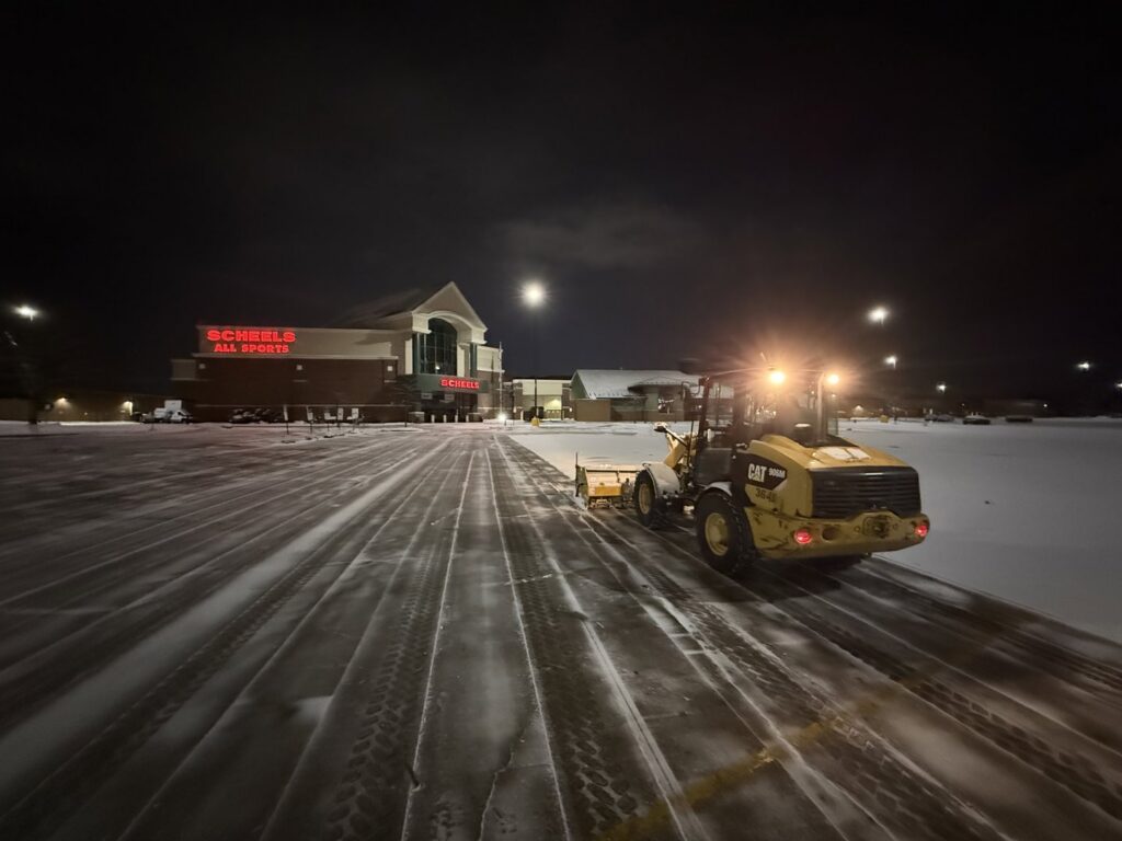 A yellow CAT loader actively plowing a large commercial parking lot at night for Appleton Snow Removal in Appleton, WI.