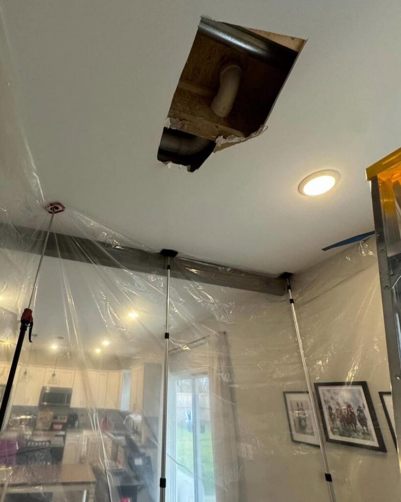 A damaged ceiling with a hole and exposed pipes, showing containment setup for water damage repair by KY Water Damage Restoration in Georgetown, KY.