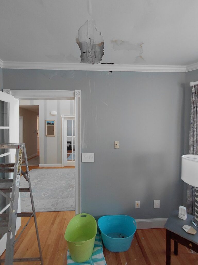 A ceiling with a large hole, water stains, and buckets, showing active water damage for PuroClean of Strafford County in Nottingham, NH.