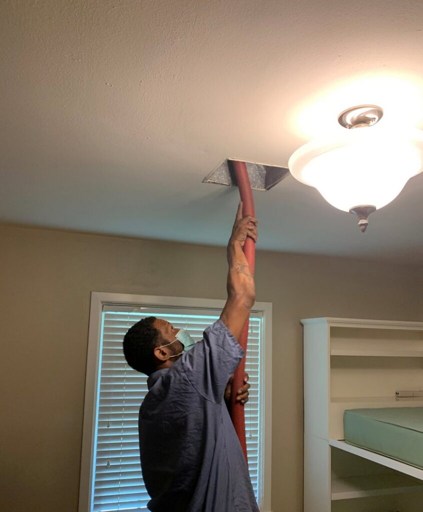 A technician using a hose to remove moisture or mold from a ceiling vent during water damage remediation by Service Professionals in Edmond, OK.