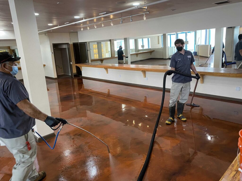 Certified Restoration crew cleaning and sanitizing a water-damaged floor in a large commercial space in San Diego, CA