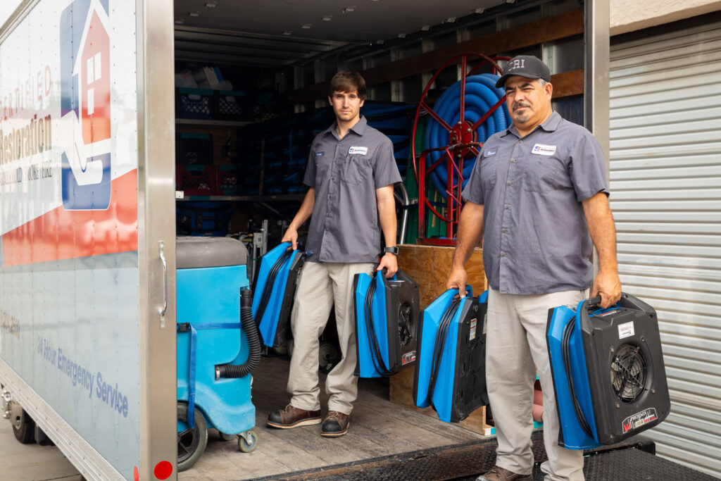 Certified Restoration technicians carrying air movers from a service truck for a water damage job in San Diego, CA