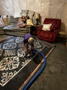A child operating a carpet cleaning wand to clean a patterned rug in a living area for FM Cleaning in West Fargo, ND.