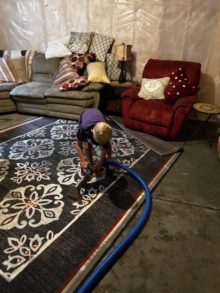 A child operating a carpet cleaning wand to clean a patterned rug in a living area for FM Cleaning in West Fargo, ND.