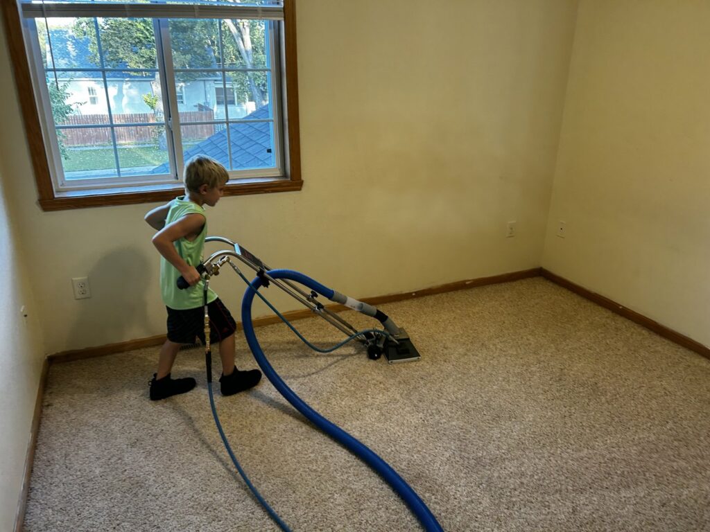A child operating a carpet cleaning wand on a light brown carpeted floor for FM Cleaning in West Fargo, ND.