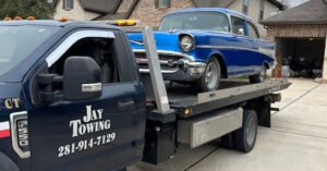 A classic blue car being transported on a flatbed tow truck by Jay Towing Services in Houston, TX.