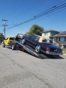 A classic brown car is being loaded onto a flatbed tow truck by S&F Towing in Oakland, CA.