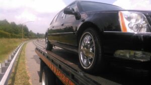 A classic Cadillac convertible being transported on a flatbed tow truck at night by Baltimore Towing Service LLC in Owings Mills, MD.