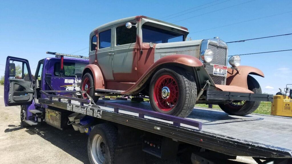 An old classic car being transported on a flatbed tow truck by Idaho State Towing and Recovery in Caldwell, ID.