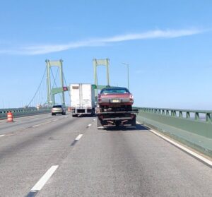 A classic car being towed on a flatbed tow truck by Craig's Towing & Recovery across a bridge in New Castle, DE.
