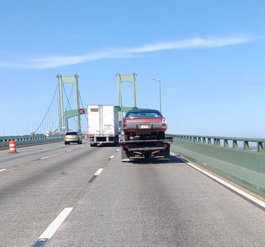 A classic car being towed on a flatbed tow truck by Craig's Towing & Recovery across a bridge in New Castle, DE.